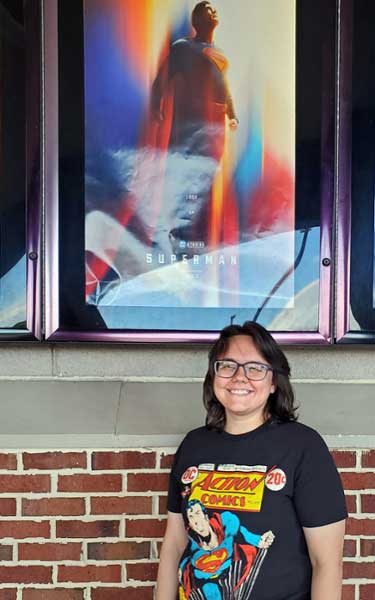 Dr. Heather Ness-Maddox poses with the Superman (2025) movie poster outside of a theater.